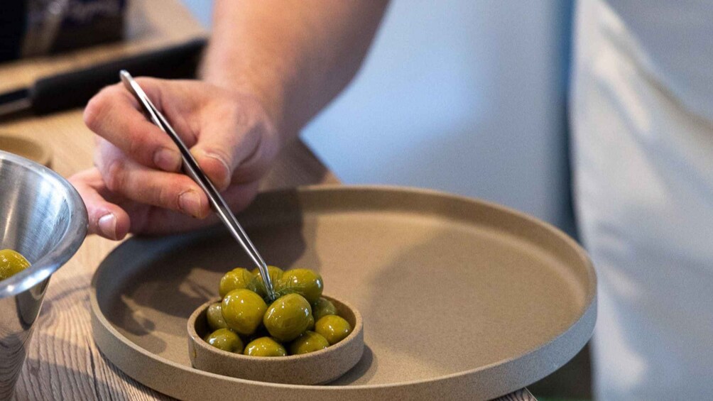 Iemand gebruikt tangen om groene olijven in een schaal op een bord te verplaatsen. 3