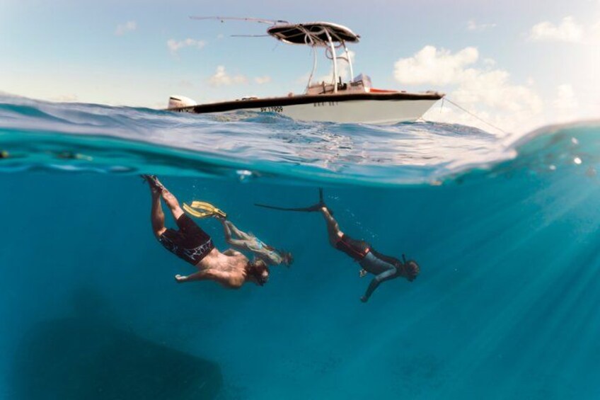 Two people swimming underwater with a boat in the background. 2