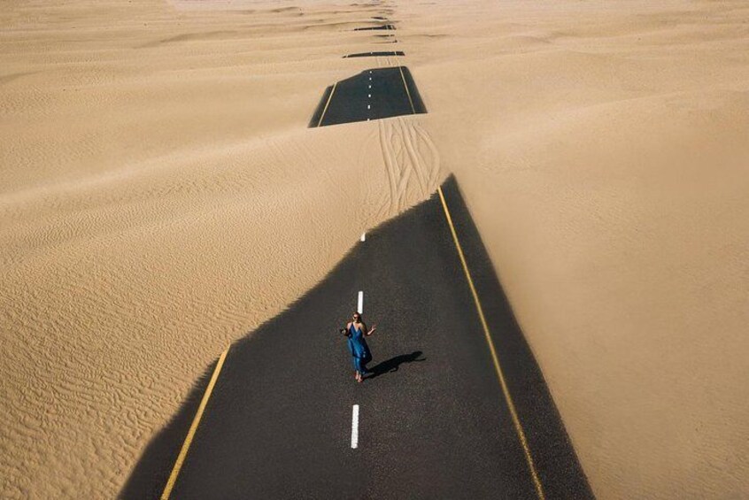 A person standing on a road in a desert with sand dunes on either side. 2