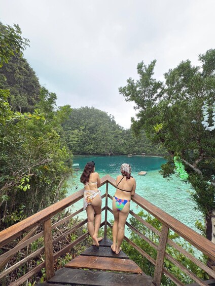 Two people standing on a wooden staircase overlooking a turquoise body of water with boats. 5