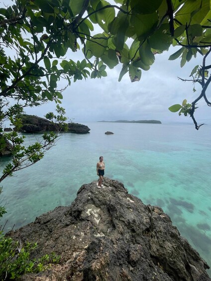 A person standing on a rocky outcrop overlooking turquoise waters with distant islands. 4