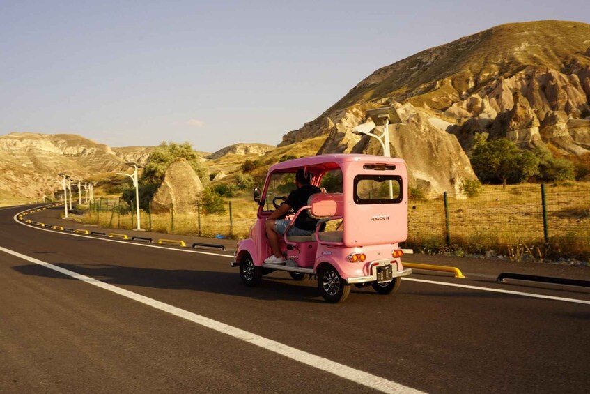 A pink three-wheeled vehicle driving on a road with a mountainous landscape in the background. 4