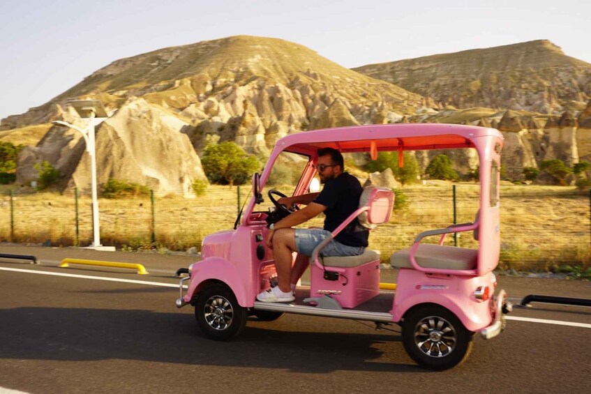 A person driving a pink golf cart on a road with mountains in the background. 5