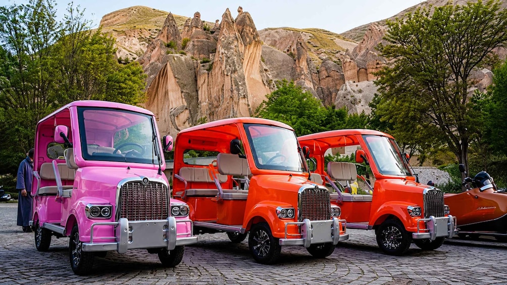 Three vintage trucks parked on a cobblestone street with a mountainous backdrop. 1