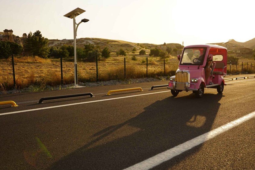A pink vehicle driving on a road with a solar street lamp and a fence in the background. 2