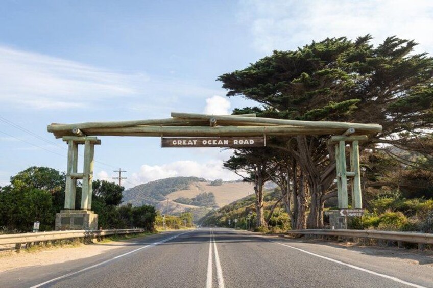 A road with a wooden archway labeled 'Great Ocean Road' and a view of the landscape in the distance. 4