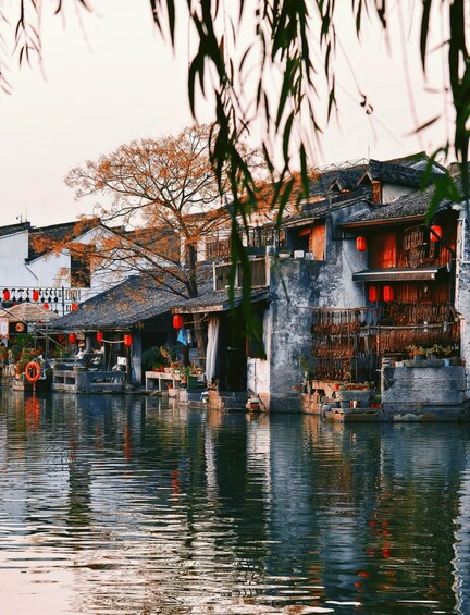 A traditional Chinese water village with buildings on stilts over the water, surrounded by trees with autumn leaves. 5
