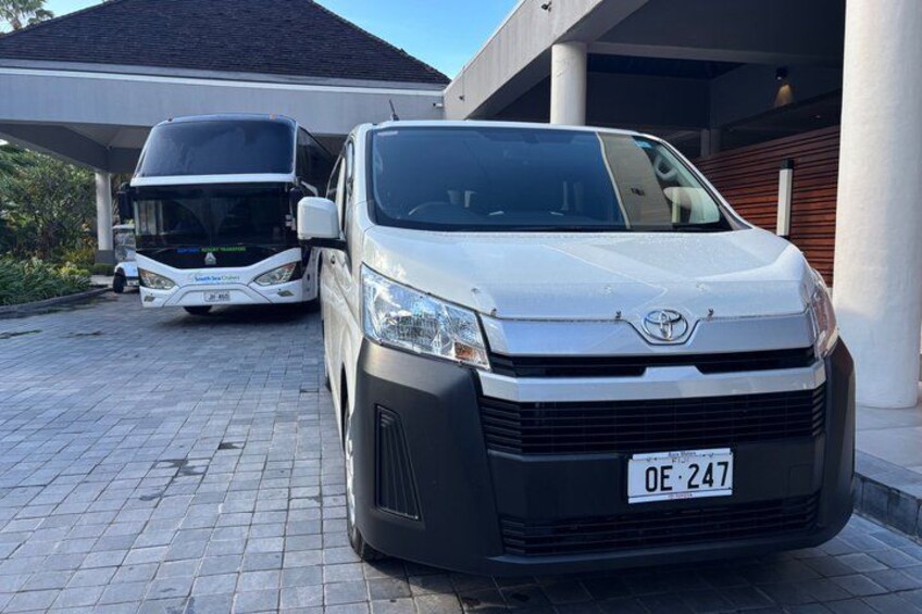 A white Toyota van parked in front of a building with a bus in the background. 4