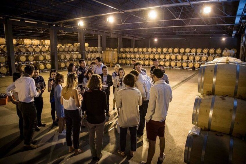 A group of people in a warehouse with large wooden barrels. 2