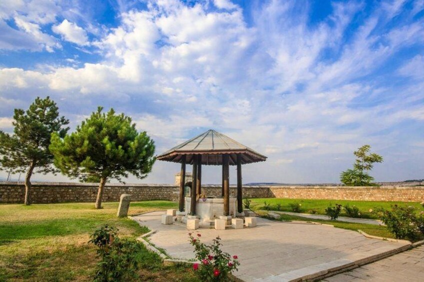 A gazebo in a park with a stone wall and trees in the background. 4
