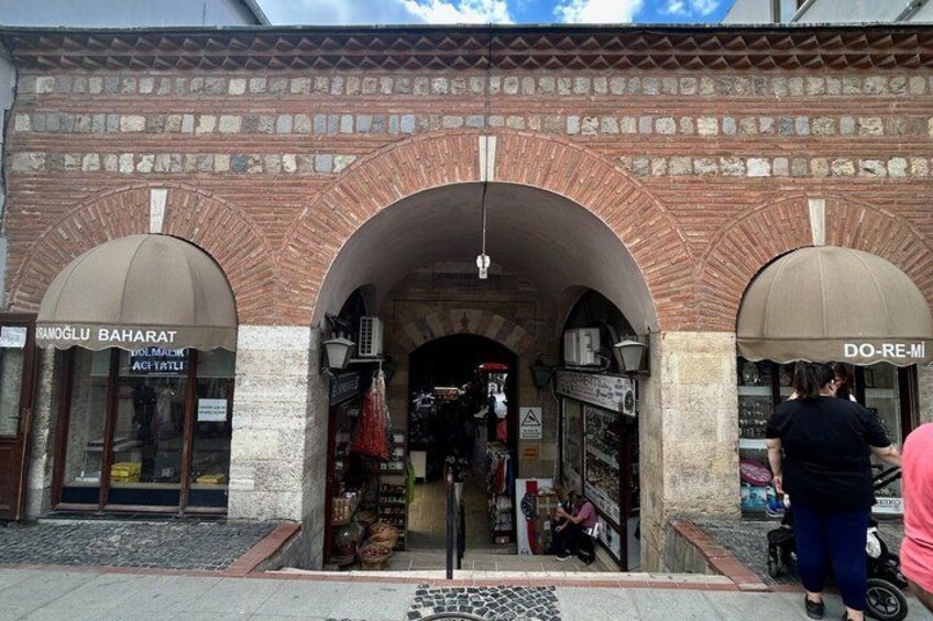 A brick building with arched entrances, a sign for 'BIRDAK' and 'DO RE MI' on the right, and a person pushing a stroller on the right side. 5