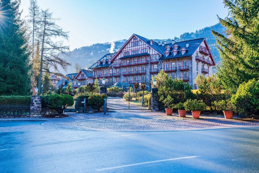 A large, multi-story building with a traditional Alpine architectural style, surrounded by lush greenery and mountains in the background. 4