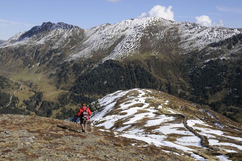 A hiker on a snow-covered mountain trail with a forested valley in the background. 3