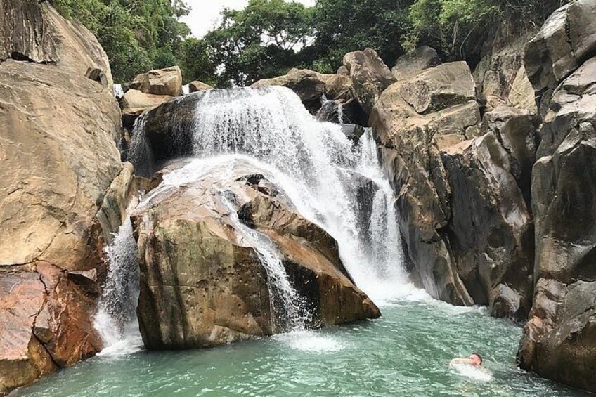 A waterfall cascading over large rocks into a pool of water, surrounded by dense greenery. 3