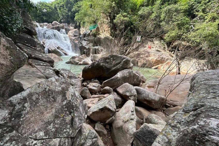 A waterfall surrounded by large rocks and greenery. 1
