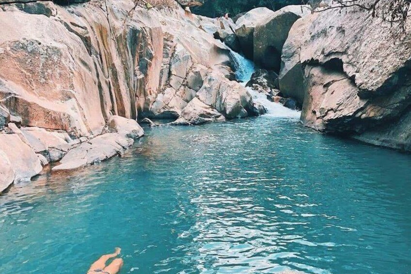 A natural pool with clear water, surrounded by rocky terrain and a small waterfall. 5