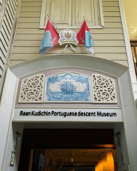 Indgangen til Baan Kudichin Museum med portugisisk baggrund, med et dekorativt skilt der viser et skib og indviklede mønstre. 3