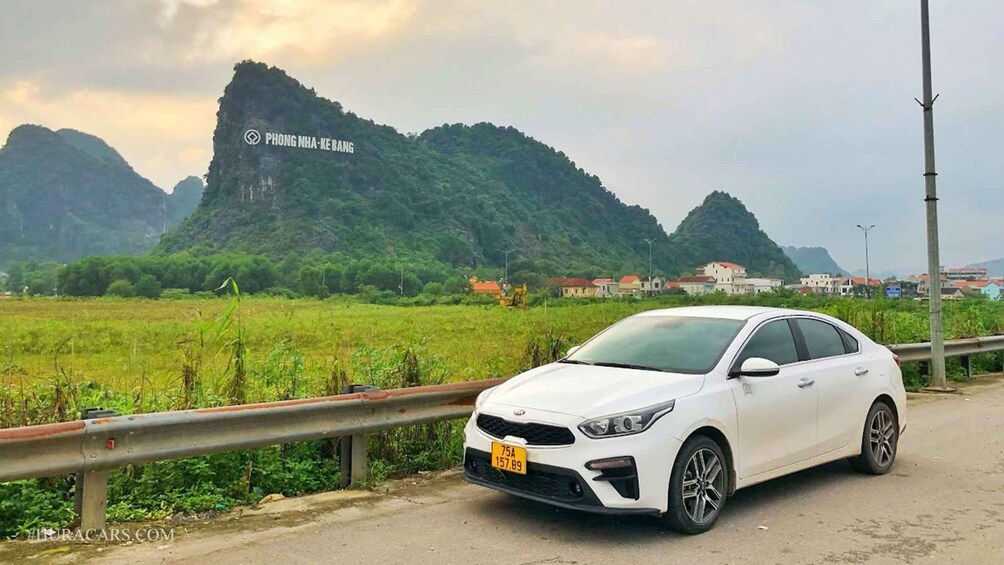 A white car parked on a roadside with a mountainous landscape in the background. 2