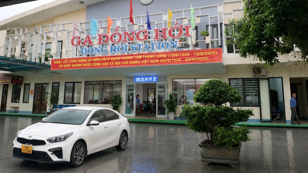 A building with a sign reading 'GA BONG HOI DONG HOISTATION' and a white car parked in front. 1