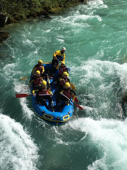 En gruppe mennesker i en blå gummibåd navigerer gennem en flod med hvide rapids. 2