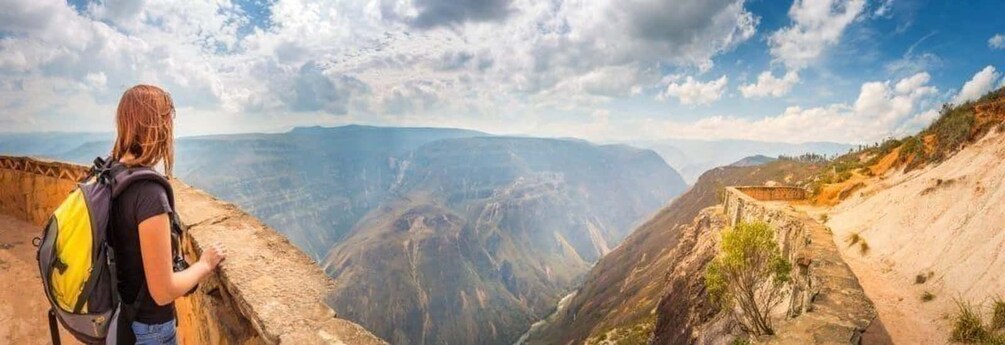 A person with a backpack overlooking a canyon with layered rock formations and a clear sky. 1
