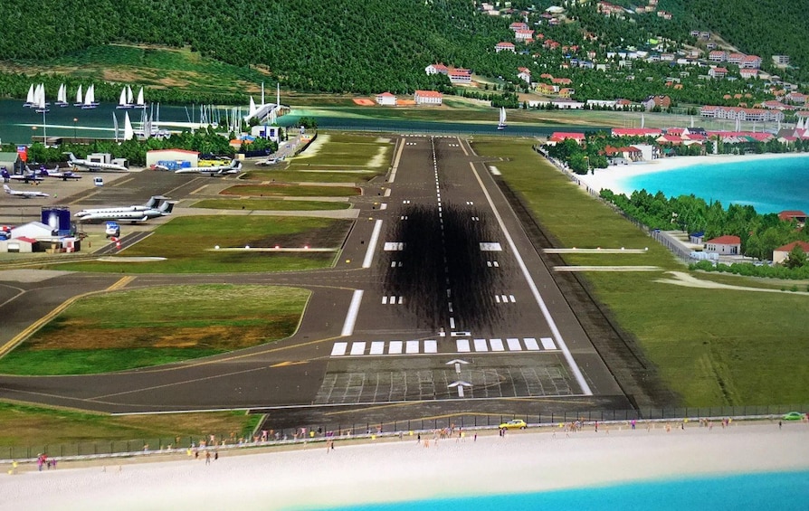 An airport runway with airplanes, a beach, and a coastal town in the background. 3