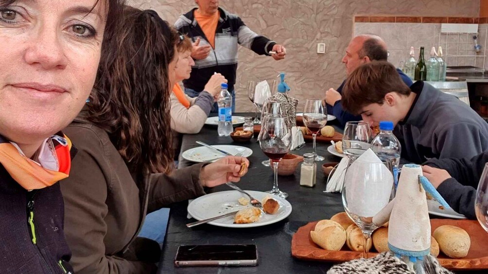 A group of people dining at a restaurant with plates of food, glasses of wine, and a bottle of water on the table. 5