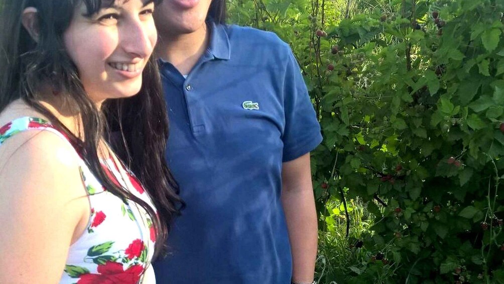 Two people standing outdoors with dense green foliage in the background. 3