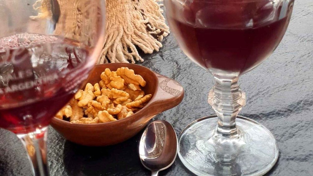 A bowl of walnuts, a wine glass with red wine, and a spoon on a dark surface. 4