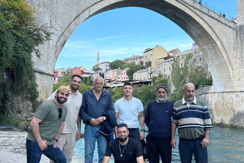 A group of people standing under a stone bridge with buildings in the background. 3