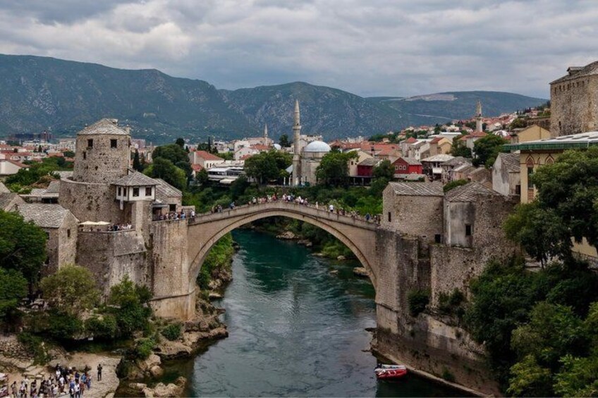 A stone bridge over a river, surrounded by historic buildings and a mosque. 4