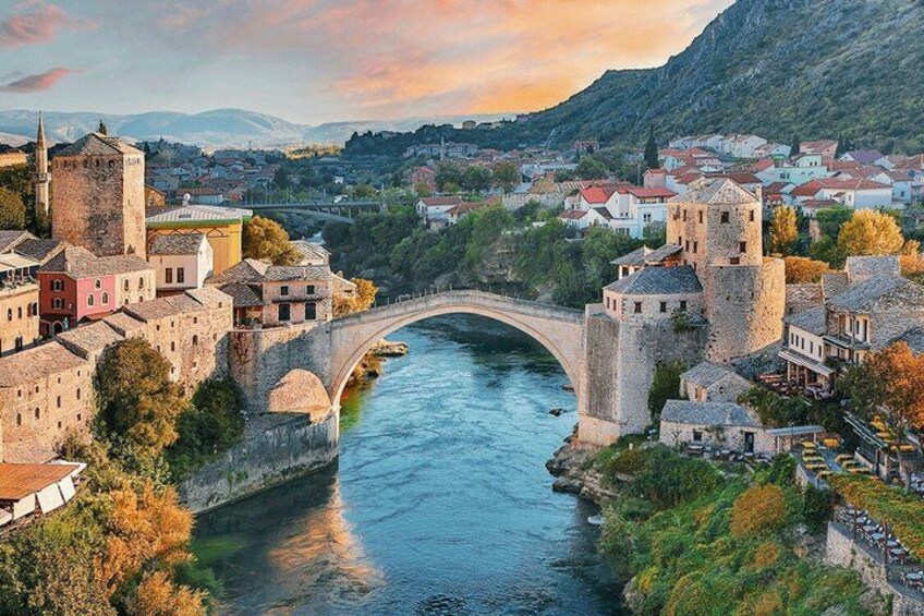 A river with a stone bridge, historic buildings, and a mountainous backdrop. 1