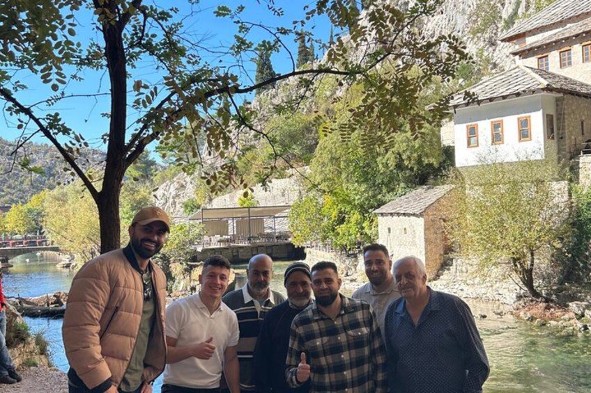A group of people standing by a river with buildings and trees in the background. 2