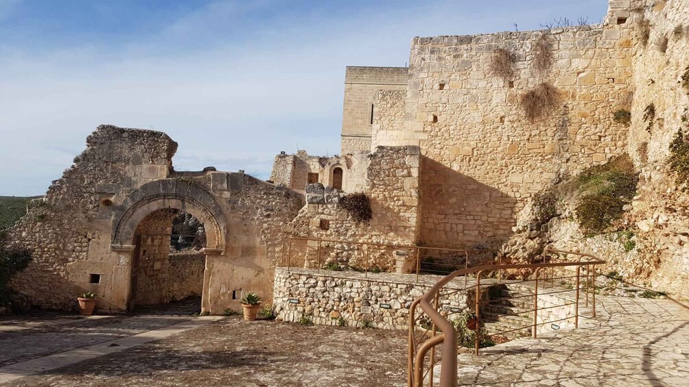 An ancient stone fortress with a large arched entrance, a staircase, and a small garden area with potted plants. 5