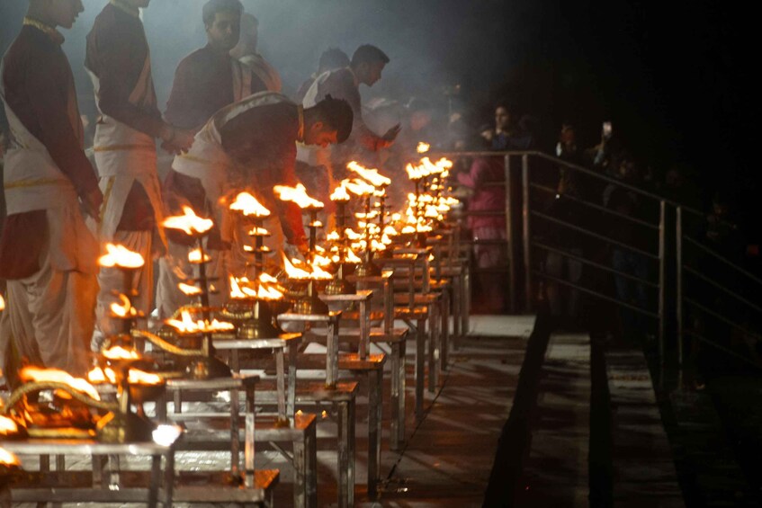 En rad tända oljelampor, troligen en del av en religiös ceremoni, med människor i traditionella kläder som står runt omkring dem. 4