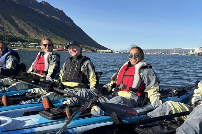 Three people in kayaks on a calm body of water with mountains in the background. 1