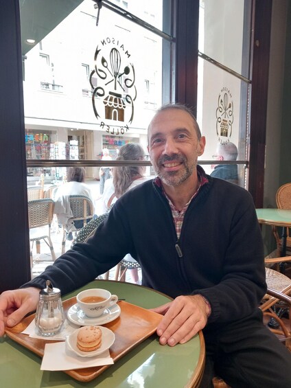 A man sitting at a table with a coffee cup, a salt shaker, and a pastry. 3