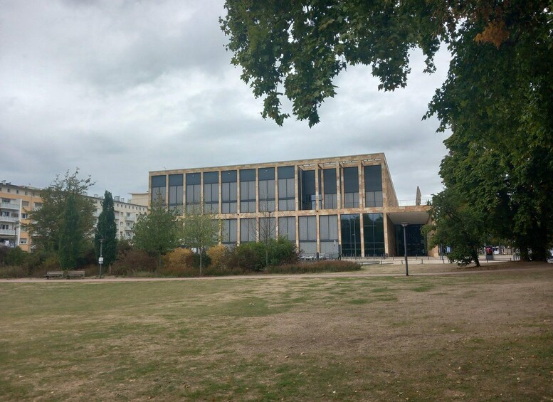 A modern building with large windows, surrounded by a grassy field and trees. 5