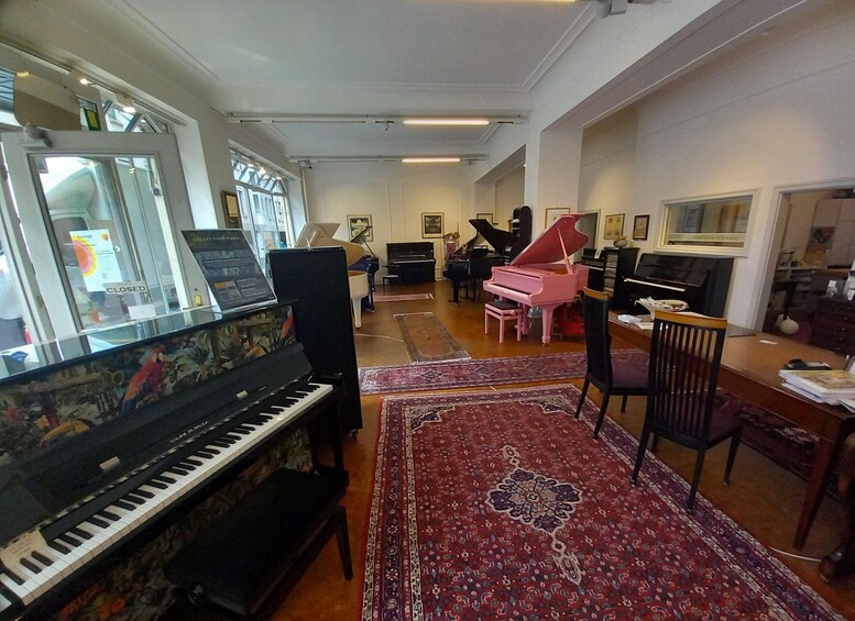 A living room with a grand piano, a pink grand piano, a black piano, a television, and a red patterned rug. 1
