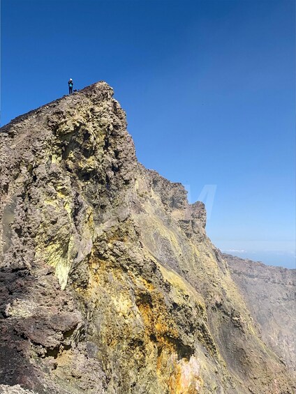 A person standing on a rocky mountain peak with a clear blue sky. 2