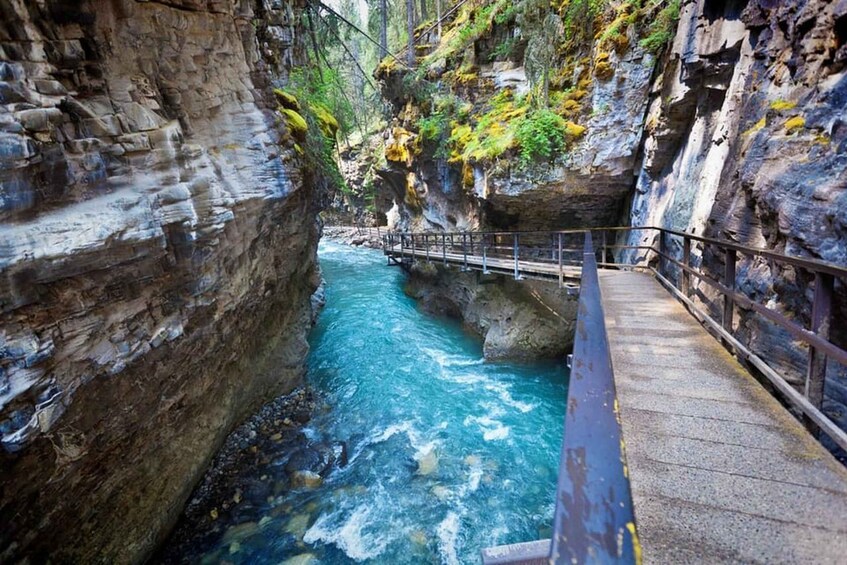 Un défilé rocheux traversé par une rivière aux eaux d’un bleu limpide, un pont en bois et une rambarde en métal. 2