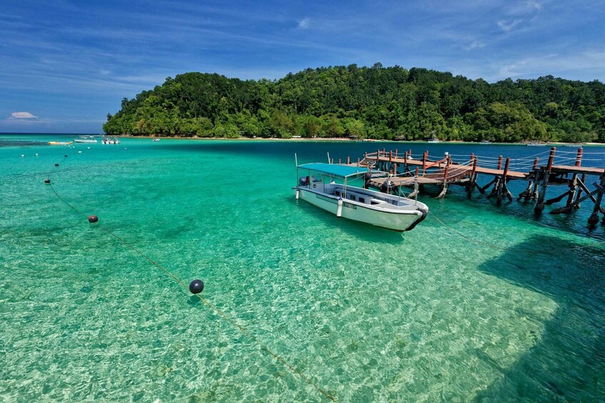A boat docked at a pier with clear turquoise water and a forested island in the background. 2