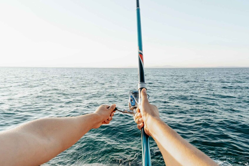 A person holding a fishing rod over the ocean. 1