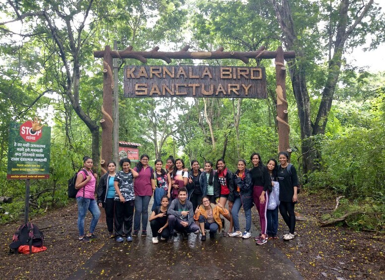 Eine Gruppe von Personen posiert vor einem Schild mit der Aufschrift 'Karnataka Bird Sanctuary', umgeben von Bäumen. 1
