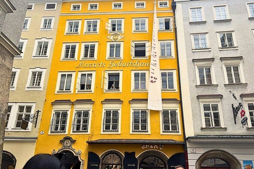 A yellow building with the sign 'Mozarts Geburtshaus' and a white flag. 2