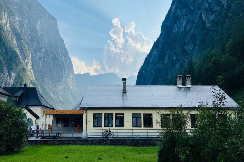 A mountain lodge with a white facade, surrounded by lush greenery and steep cliffs. 4