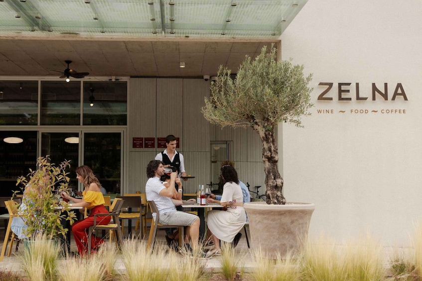 An outdoor seating area of ZELNA restaurant with patrons dining and a waiter attending to them. 4
