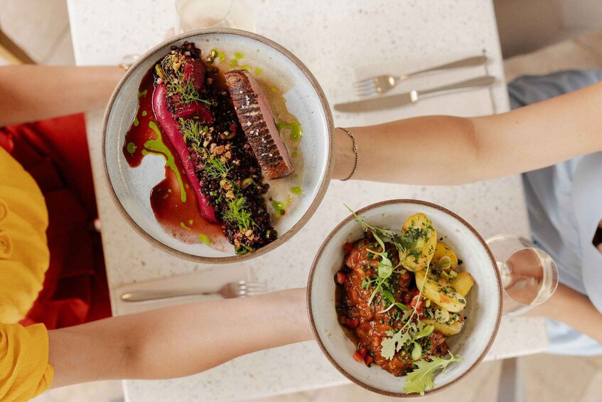 Two people holding plates of food, one with a steak and the other with a potato dish. 2