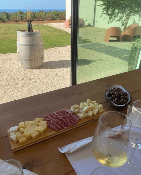 A wooden table with a cheese board, charcuterie, olives, and wine glasses. 3