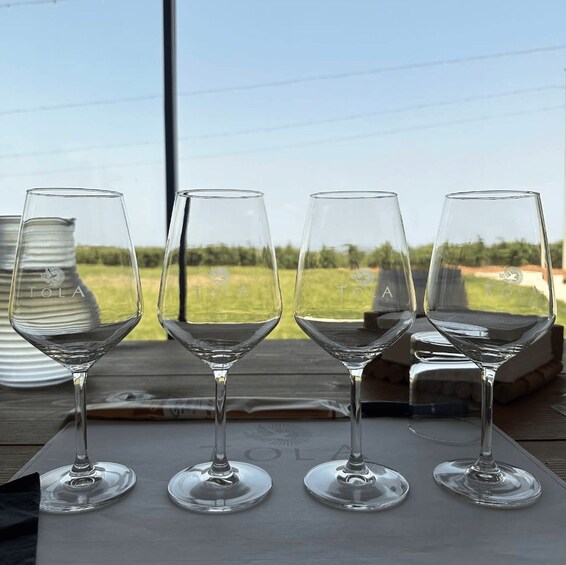 Four wine glasses on a table with a view of a grassy field and a building in the background. 2